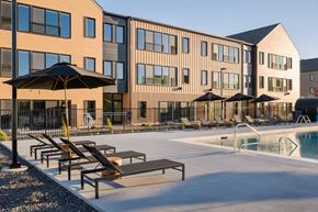 Idaho Falls apartment for rent - A pool area with sun loungers and umbrellas in front of a building.
