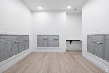 A room with white walls and wooden flooring, featuring a row of grey lockers on the left and a bench on the right.