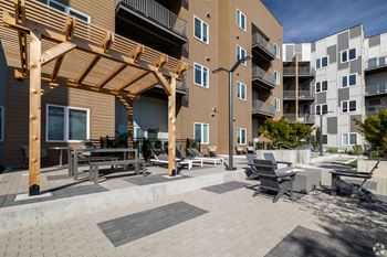 A patio area with a wooden pergola and seating area in front of apartment buildings.