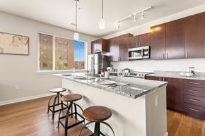 Denver apartment for rent - View of the kitchen with a granite island with barstool seating and pendant lighting at Sylvan Uptown, Denver