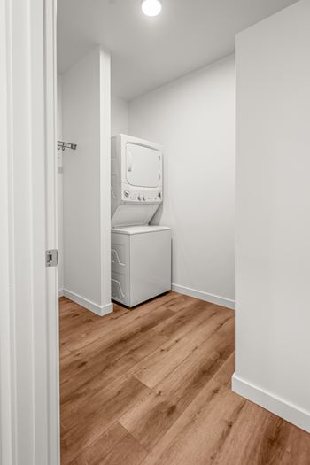A white washing machine is in a small room with wooden floors.