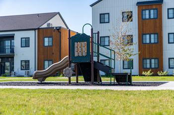 A playground with a slide and a bench in front of a building.