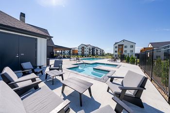 A sunny day at a poolside with chairs and a table.