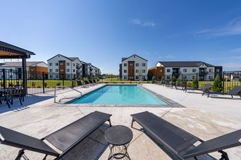 A swimming pool surrounded by lounge chairs and buildings in the background.