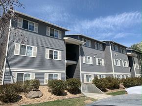 Boise apartment for rent - a gray apartment building with white windows and a blue sky in the background