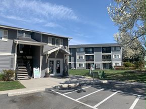 Boise apartment for rent - a gray apartment building with a lawn and trees in front of it