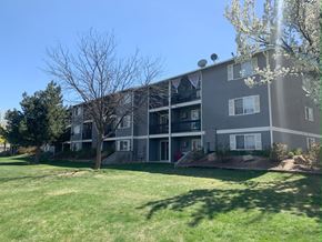 Boise apartment for rent - a gray apartment building with a green lawn and trees