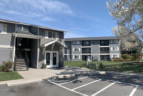 Boise apartment for rent - A building with a grey facade and a white door is surrounded by a parking lot.