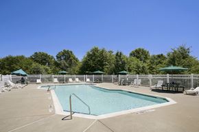 Middletown apartment for rent - a pool with chairs and umbrellas and trees in the background at Boulder Pointe Apartments in Middletown, NY 10940
