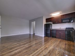 Wood-Ridge apartment for rent - an empty living room with wooden floors and a kitchen with black appliances