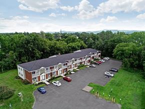 Cohoes apartment for rent - an aerial view of a red brick building with a gray roof and a parking lot in front