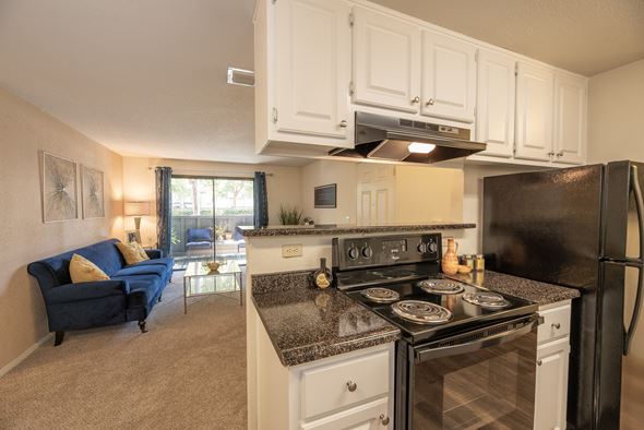 Rancho Cordova apartment for rent - A kitchen with black appliances and a blue couch in the living room at Bishop's Court Apartments, California, 95670