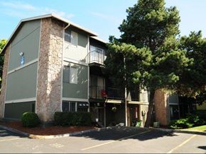 Portland apartment for rent - A building with a stone pillar and balconies is surrounded by trees and bushes.