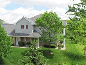 West Allis townhouse for rent - A house with a grey roof and a white door is surrounded by green trees.