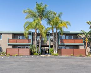 Lemon Grove apartment for rent - A building with a parking lot in front of it and palm trees in the background.