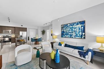 Pembroke Pines apartment for rent - A modern living room with a white sofa, a blue and white abstract painting on the wall, and a black coffee table with yellow vases.
