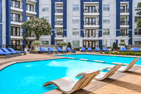 Dallas apartment for rent - A large swimming pool with lounge chairs in front of a multi-story apartment building.