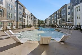Charlotte apartment for rent - A pool surrounded by white lounge chairs in front of apartment buildings.