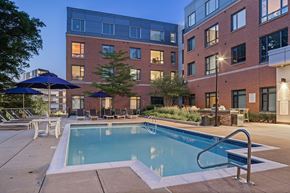 Boston apartment for rent - A swimming pool surrounded by lounge chairs and umbrellas in front of a brick building.