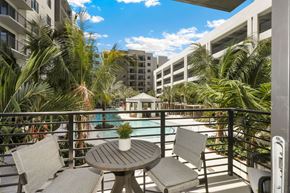 Boca Raton apartment for rent - A table with chairs is on a balcony with a pool and palm trees in the background.