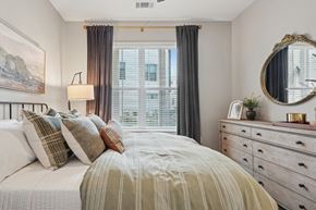 Charlotte apartment for rent - A bedroom with a large bed, a dresser with a mirror, and a window with curtains.