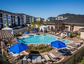 Frederick apartment for rent - A pool surrounded by chairs and umbrellas with apartment buildings in the background.