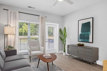 Raleigh apartment for rent - A living room with a grey couch, a wooden coffee table, a grey cabinet, a white chair, a potted plant, and a painting on the wall.