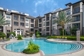Orlando apartment for rent - A large swimming pool surrounded by lounge chairs and palm trees in front of apartment buildings.