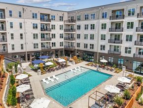Charlotte apartment for rent - A large swimming pool surrounded by lounge chairs and umbrellas in front of a multi-story apartment building.