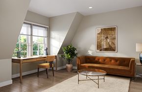 Florham Park apartment for rent - A living room with a brown couch, a desk with a chair, a potted plant, and a framed picture on the wall.