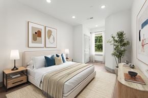 Roseland triplex for rent - A bedroom with a large bed, a nightstand with a lamp, and two framed pictures on the wall.