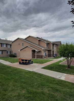 Laramie apartment for rent - A house with a brown roof and a white door is surrounded by a green lawn.