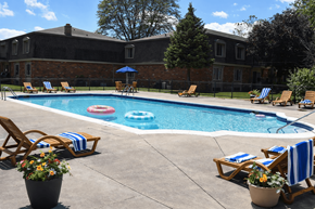 Southfield townhouse for rent - A pool surrounded by chairs and umbrellas with a building in the background.