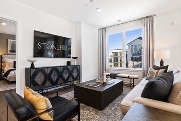 West Orange apartment for rent - A living room with a black leather couch and a large TV displaying the word "STONEHILL".