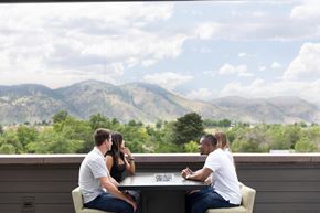 Golden apartment for rent - Three people sitting at a table with a mountainous landscape in the background.