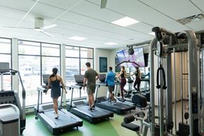 Golden apartment for rent - A gym with people exercising and a TV screen.