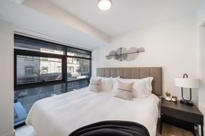 Vancouver apartment for rent - A bedroom with a large bed and a window overlooking a cityscape.