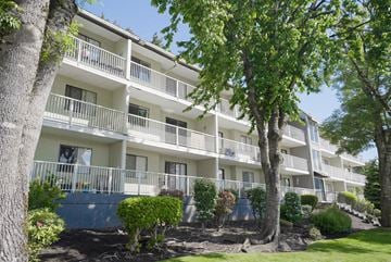Chilliwack apartment for rent - A white apartment building with balconies and trees in front.