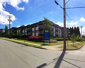 New Westminster apartment for rent - A street view of a residential area with apartment buildings and a sign for a real estate agency.