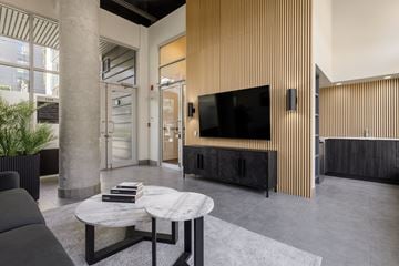 Vancouver apartment for rent - A modern living room with a black sofa, a round coffee table, and a flat screen TV mounted on a wooden cabinet.