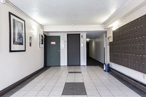 Surrey apartment for rent - A hallway with a black and white tiled floor, a door with a red sign above it, and a wall with a framed picture on it.