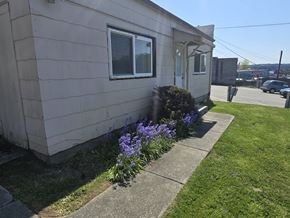 Poulsbo apartment for rent - A beige house with a window and a bush with purple flowers in front.