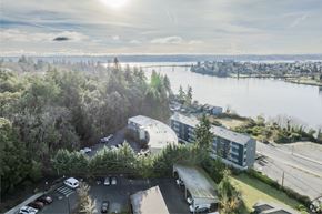 Bremerton apartment for rent - A sunny day at a parking lot with a large building and a body of water in the background.