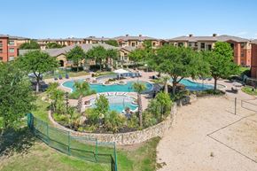 Lewisville apartment for rent - A large swimming pool surrounded by a fence and trees in a residential area.