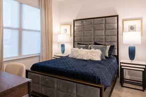Overland Park apartment for rent - a bed with blue comforter in a bedroom with two lamps and a large window at The Apex at CityPlace, Overland Park, 66210