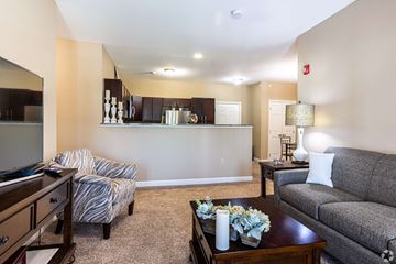 Olathe apartment for rent - A living room with a grey couch, a coffee table, and a chair with a striped cushion.