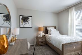 Olathe townhouse for rent - A bedroom with a large bed, a wooden nightstand, and a mirror on the wall.