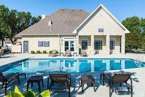Lenexa apartment for rent - A poolside lounge area with chairs and tables is in front of a house.