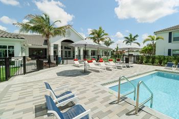 A swimming pool with lounge chairs and umbrellas in front of a house