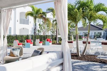 A lounge area with white curtains and chairs and palm trees in the background